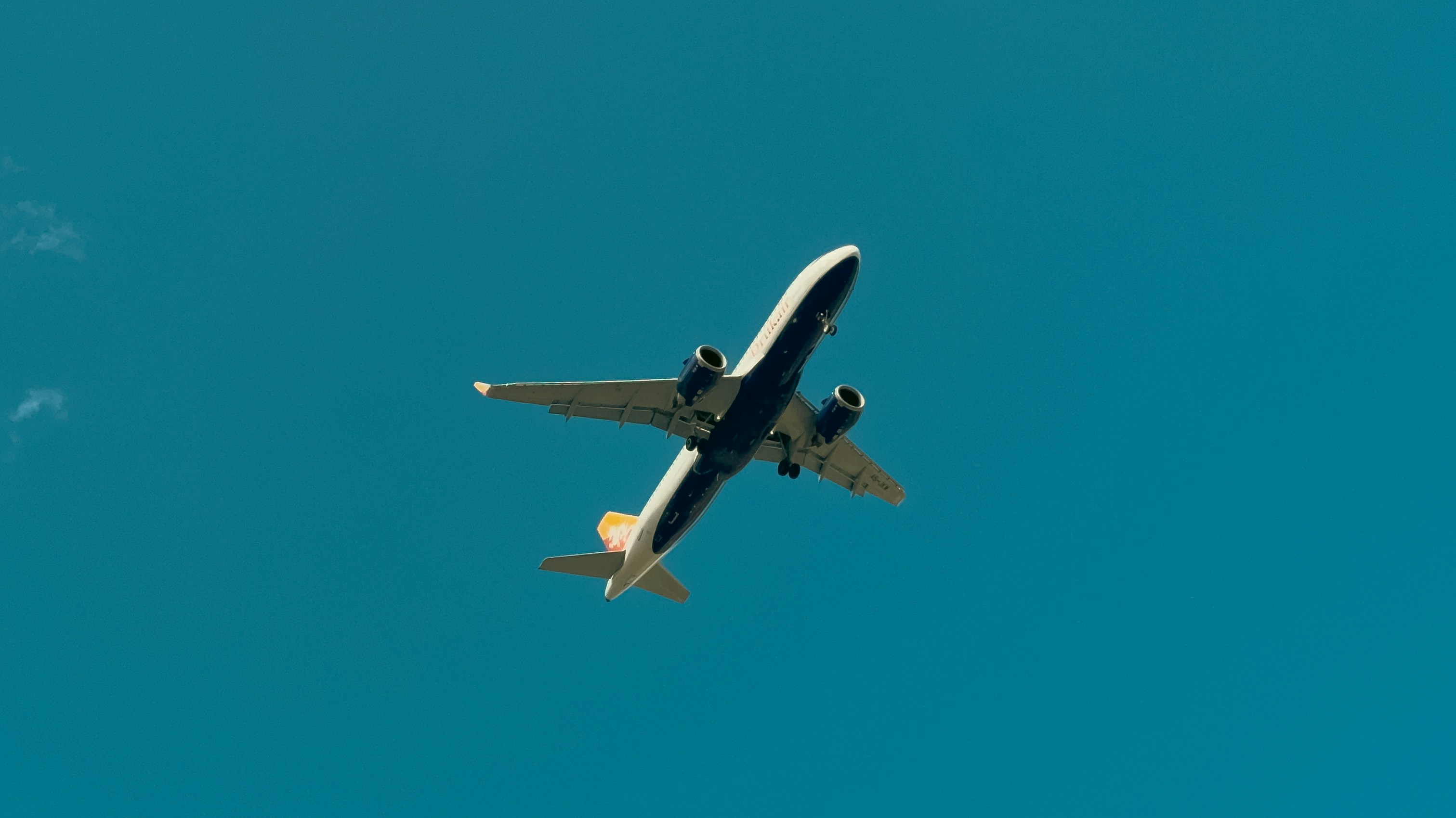 A commercial airplane soars overhead against a vivid blue sky, captured mid-descent as it approaches landing in Paro, Bhutan—one of the world's most dramatic flight paths.